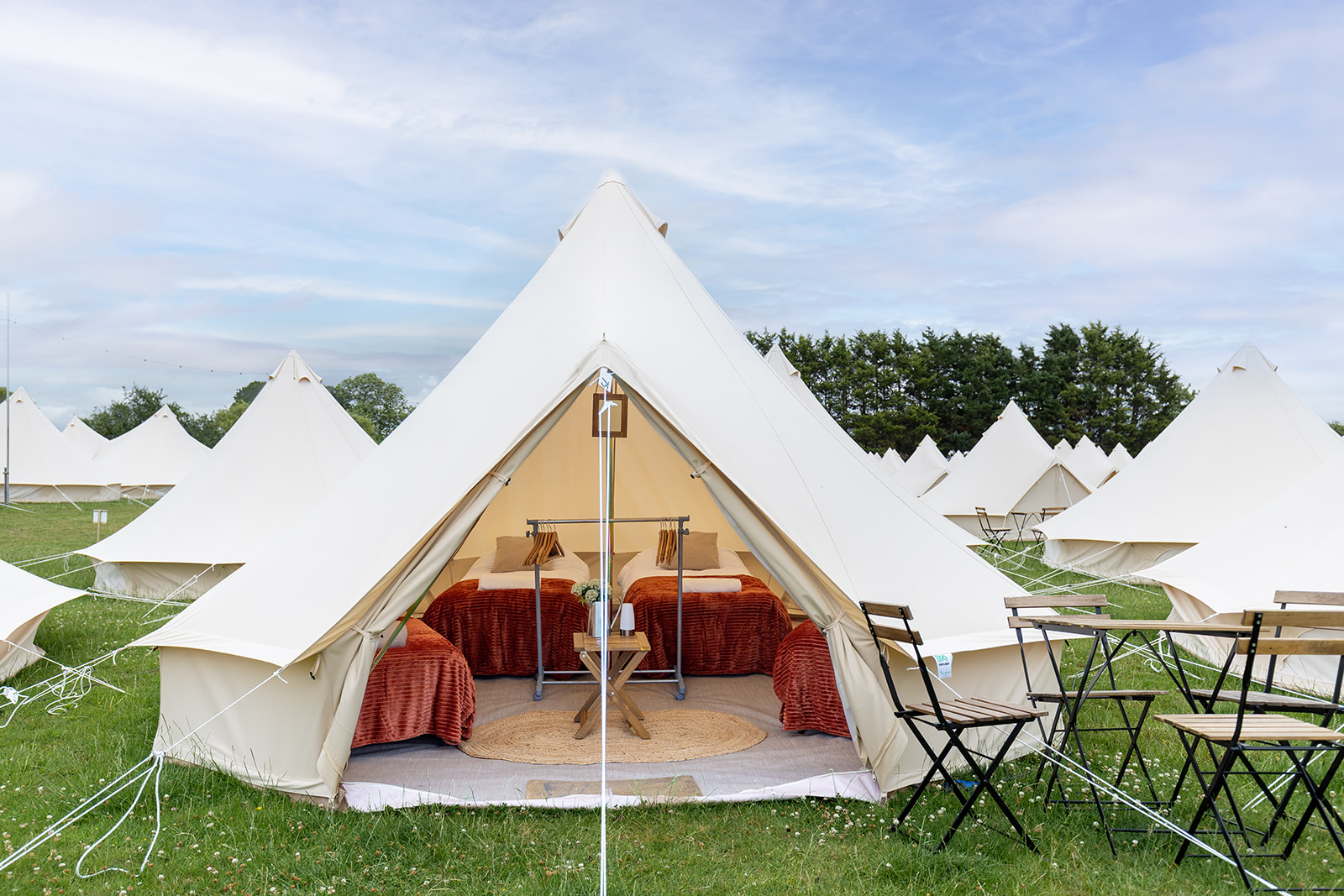 Open bell tent with four made-up beds and chairs pitched outside