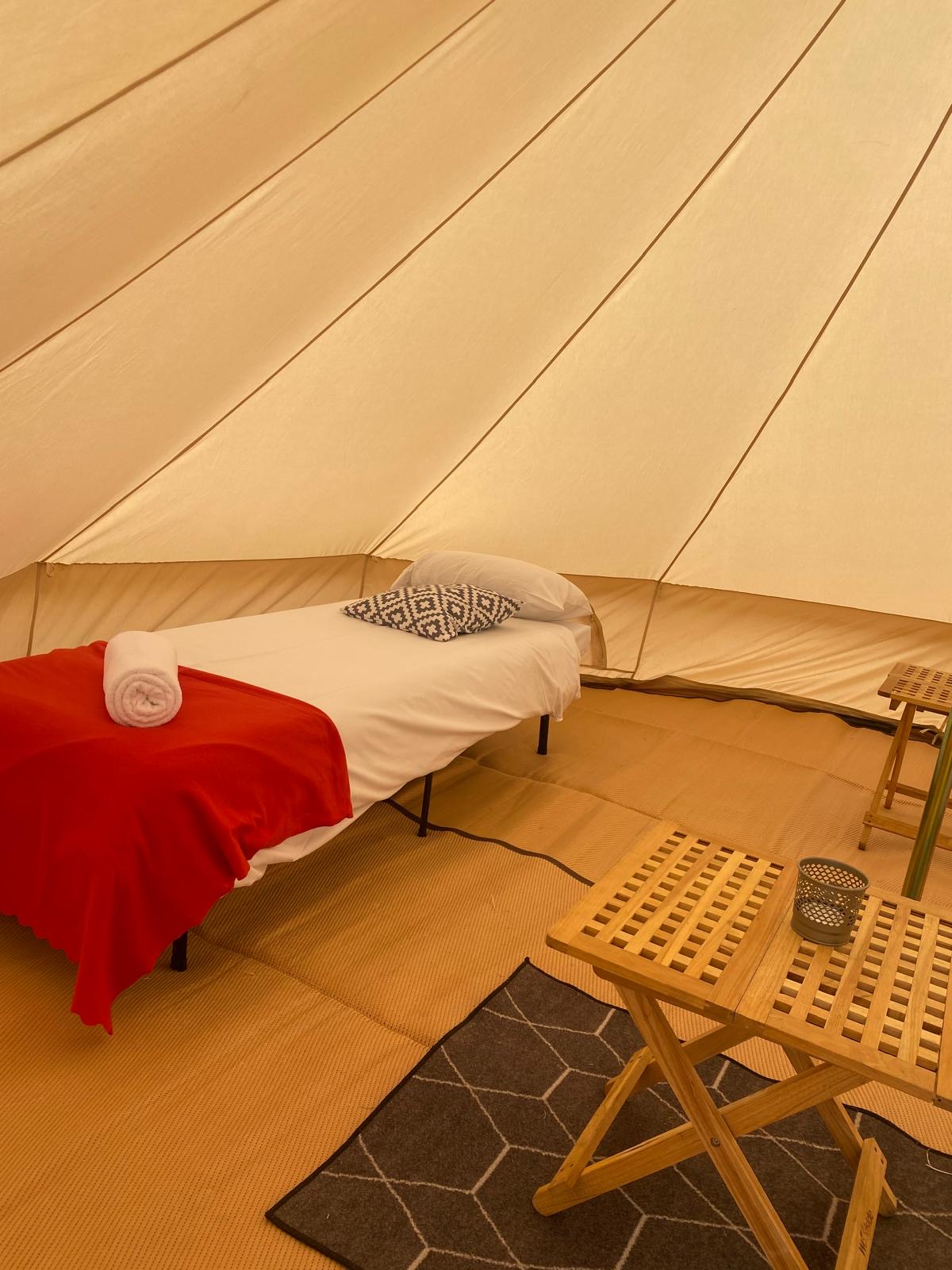 Furnished bell tent interior with a bed and wooden tables
