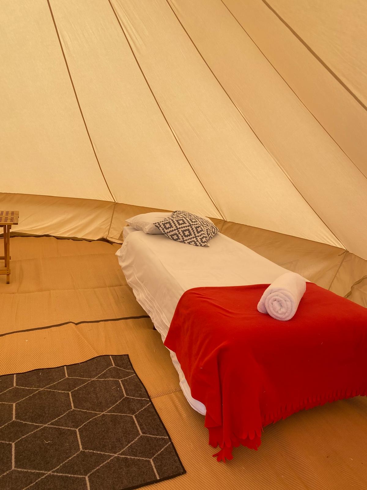 Made-up bed with red blanket and towel inside a bell tent